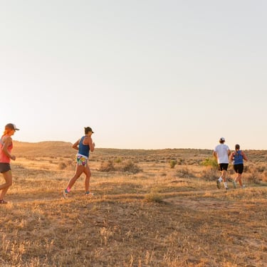 A group of athletes enjoy trail running through a golden desert landscape at sunrise.