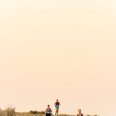 A group of female athletes running a cross country trail race through a desert at sunrise.