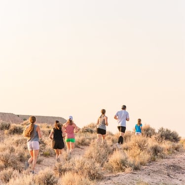A group of people trail running uphill through a desert landscape during a scenic sunrise.