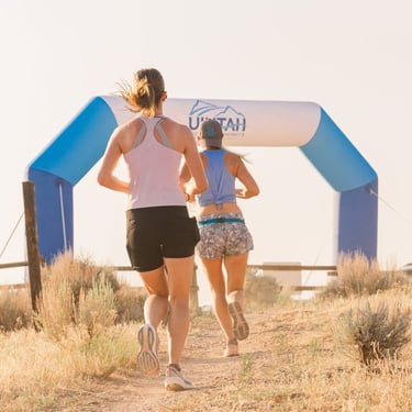 Two women trail running toward a race finish line arch in the Utah desert.