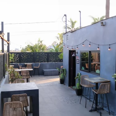 Outdoor patio area with tables, chairs, and a partial view of the building.