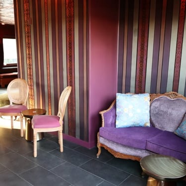 Couch with pillows in a room with striped wallpaper and decorative chairs.