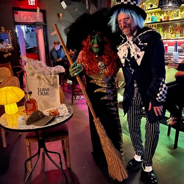 Two people in Halloween costumes, a witch and a Mad Hatter, pose in a decorated bar.