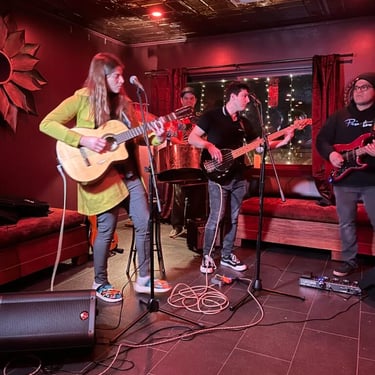  Live band performing on a small stage with a woman singing and playing guitar.