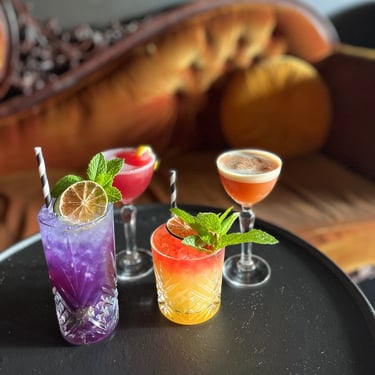 Four colorful, purple, red, orange cocktails on black table