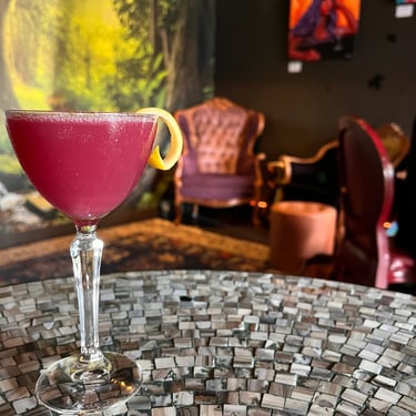 Close-up of a purple cocktail in a stemmed glass on a mosaic-tiled table