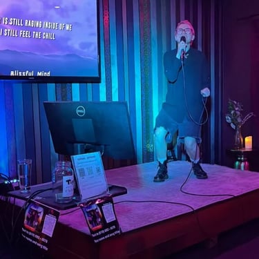 Woman singing on a small stage with a microphone and monitor displaying lyrics.