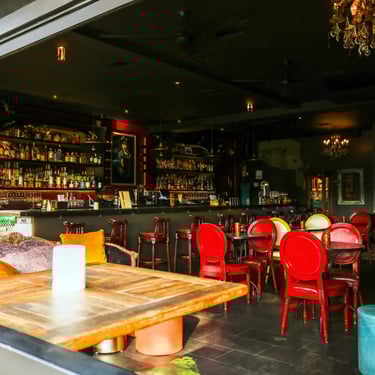 Bar interior with a large wooden table and red chairs.