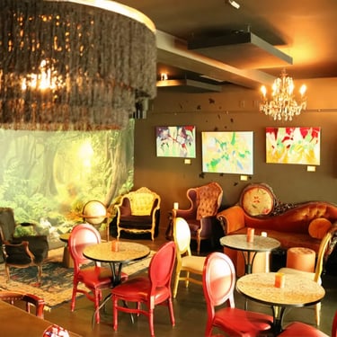 Rustic bar interior with a wooden counter, hanging lamps, and artwork on the walls.