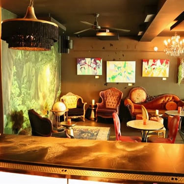  Bar interior with a chandelier, round tables, and red chairs.