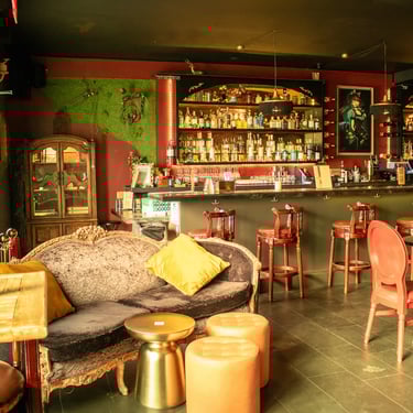 Vintage-style bar interior with a couch, chairs, and a bar counter in the background.