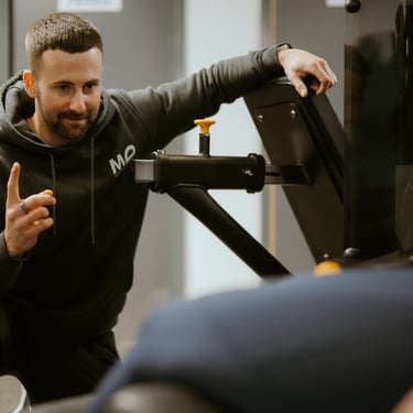 Personal trainer in hoodie coaching client on gym equipment in Leamington Spa fitness centre, focused on technique and su