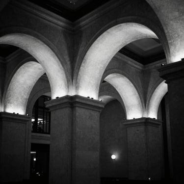 Dramatic architectural uplighting illuminating clean stone arches in a premium Manhattan venue, high contrast black and white
