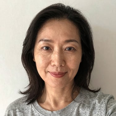 Smiling woman in workout gear holding a smoothie in a bright kitchen.