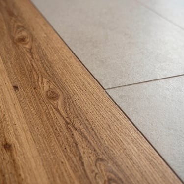 Extreme close-up of a flush transition between hand-scraped engineered hardwood and smooth tile, warm natural daylight showing grain