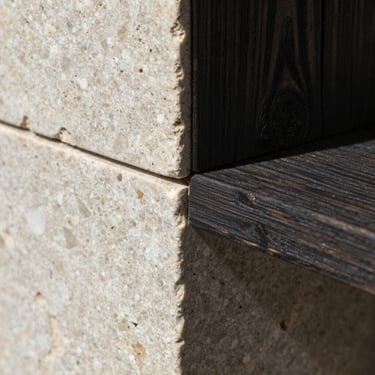 Macro detail of architectural material intersection, raw light travertine stone meeting dark charred wood, sharp geometric shadow line