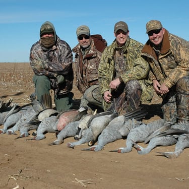 A group of hunters in camouflage with a black lab after a successful West Texas sandhill crane hunt.
