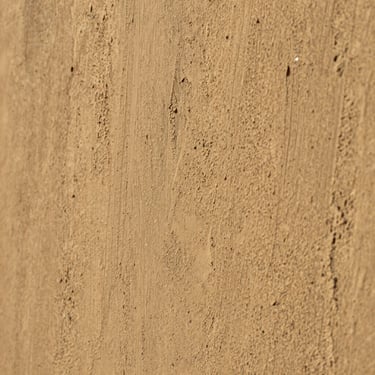 Close-up of a hand-textured decorative plaster wall in warm sand tones, catching soft natural side light, showing rich tactile depth.