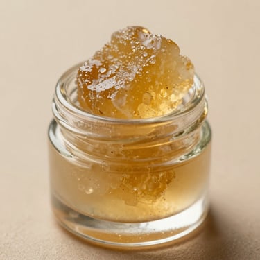 Close-up of golden, translucent live resin concentrate in a small, elegant glass jar, soft studio lighting with gentle warm highlights.
