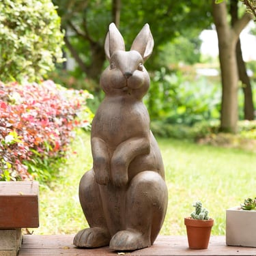 Decorative stone rabbit statue standing in a lush green garden setting.