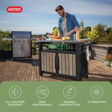 A man uses a Keter outdoor BBQ prep table and rolling kitchen cart on a patio next to a grill.