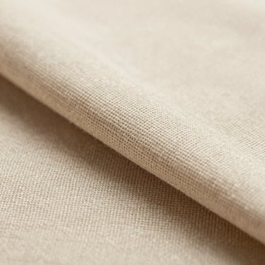 Macro close-up of natural beige linen fabric stacked neatly, soft shadows showing the organic weave texture