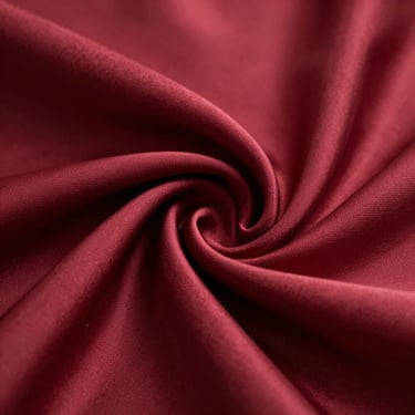 Macro close-up of folded crimson silk fabric showing rich sheen and soft light reflections, elegant editorial style
