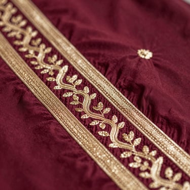 Macro shot of unstitched dress material with detailed gold embroidery on deep maroon fabric, luxury ethnic wear