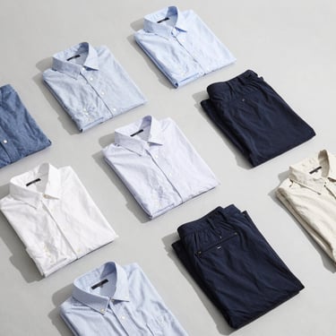 Clean flat-lay of men's button-down shirts and chinos on a light grey background, bright daylight, high contrast
