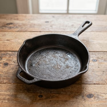 Overhead flat-lay of a seasoned cast-iron skillet on a rustic wooden table, soft natural daylight, warm tones