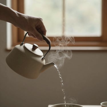 A hand pouring hot water from a minimalist ceramic kettle, steam rising gently, soft natural light