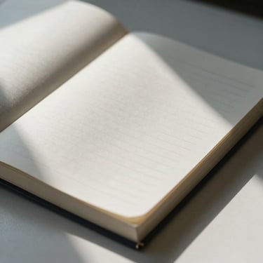 Close-up of high-quality tactile paper ledgers with sharp geometric shadows, clean workspace, cool morning daylight.