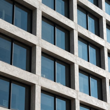 Architectural crop of a modern corporate building facade in Logan Utah, clean concrete lines and steel frames, sharp geometric shadows under cool high-contrast daylight.
