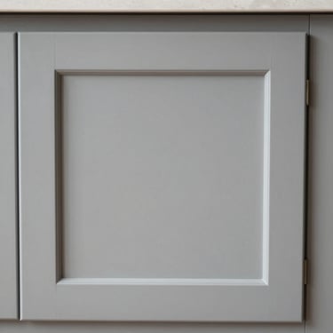 Close-up elevation of a standard shaker cabinet door, clean vertical lines, soft gray paint finish, daylight.