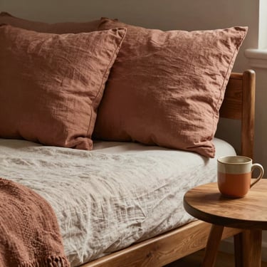 A comfortable linen daybed with soft clay-colored cushions next to a wooden side table holding a warm ceramic mug.