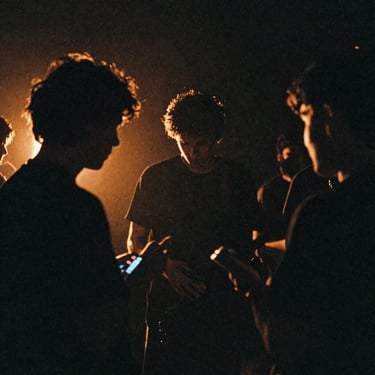 Atmospheric backstage shot of an artist in shadows, low-key neon lighting, 35mm film grain.