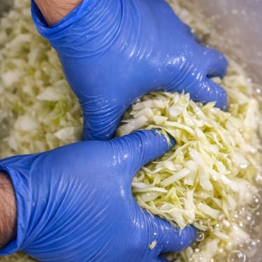 Unas manos con guantes exprimiendo una col verde, mostrando el proceso del chucrut.