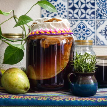 Una mesa de madera mostrando unos frascos llenos de kombucha y fruta. Mostrando el proceso de producción.