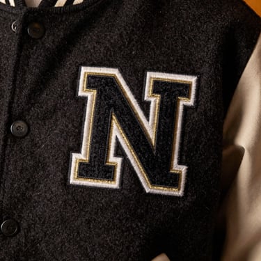 Extreme close-up of a fuzzy chenille patch with gold metallic thread accents on a heavy wool varsity jacket, warm studio lighting