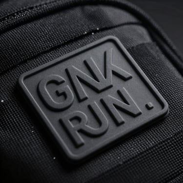 Macro shot of a molded matte PVC patch with dimensional raised lettering on a black tactical nylon backpack, high-contrast industrial lighting