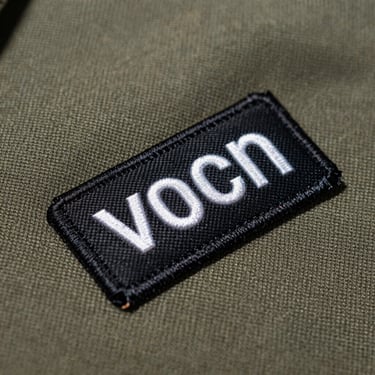 Macro photography of a crisp woven patch with clean ultra-fine lettering on a rugged canvas work shirt, sharp side shadows