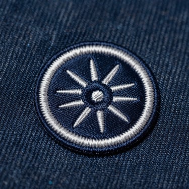 Macro studio shot of a classic embroidered patch with a thick merrowed border on heavy denim.