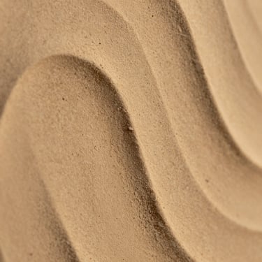 Extreme close-up macro of clayxible Sabbia wall finish under warm golden light, sandy beige tone with fine sand-grain texture and soft shadow play, semi-matte surface
