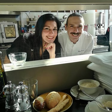 Clara Mennella in cucina insieme a uno chef durante la preparazione di un piatto