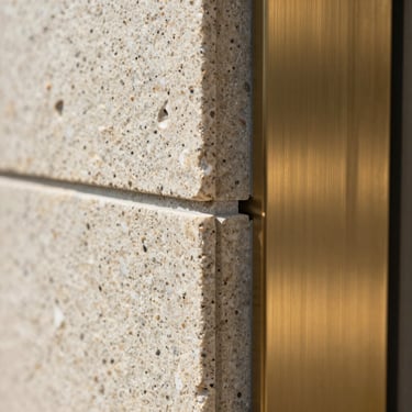 Macro detail shot of flawless joint alignment between textured basalt stone tiles and brushed brass profile, bright daylight.