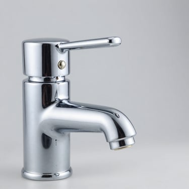 Close-up of a chrome-plated brass water faucet with crisp metallic reflections on a neutral grey background