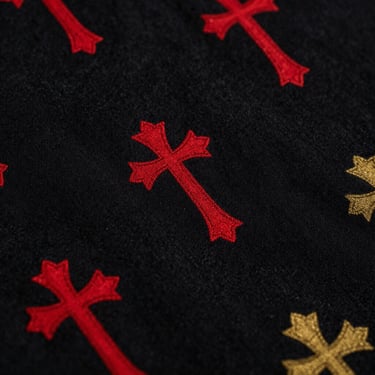 Dramatic low-key close-up of heavy-weight black cotton fabric showing sharp texture of a crimson and gold printed cross motif, side lighting