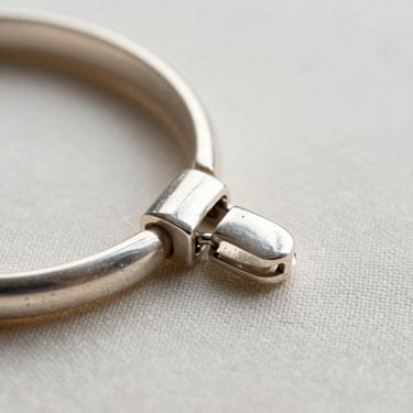Macro detail of a silver bracelet clasp on a pale linen surface, north-facing daylight illuminating the joinery and surface texture, high contrast edges, no props
