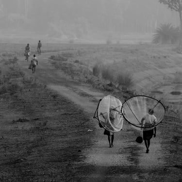 A black and white picture of some fisher women forwarding towards theri work with nets on back.