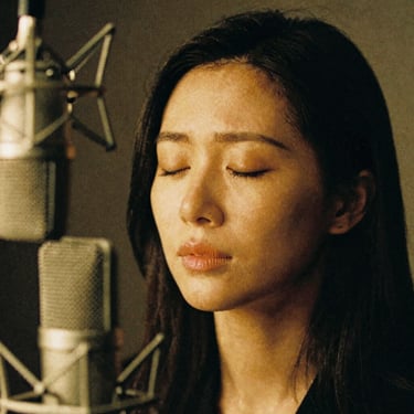 Intimate close-up portrait of a female voice actress with closed eyes, expressing emotion in front of a studio mic, moody golden lighting, 35mm film grain.